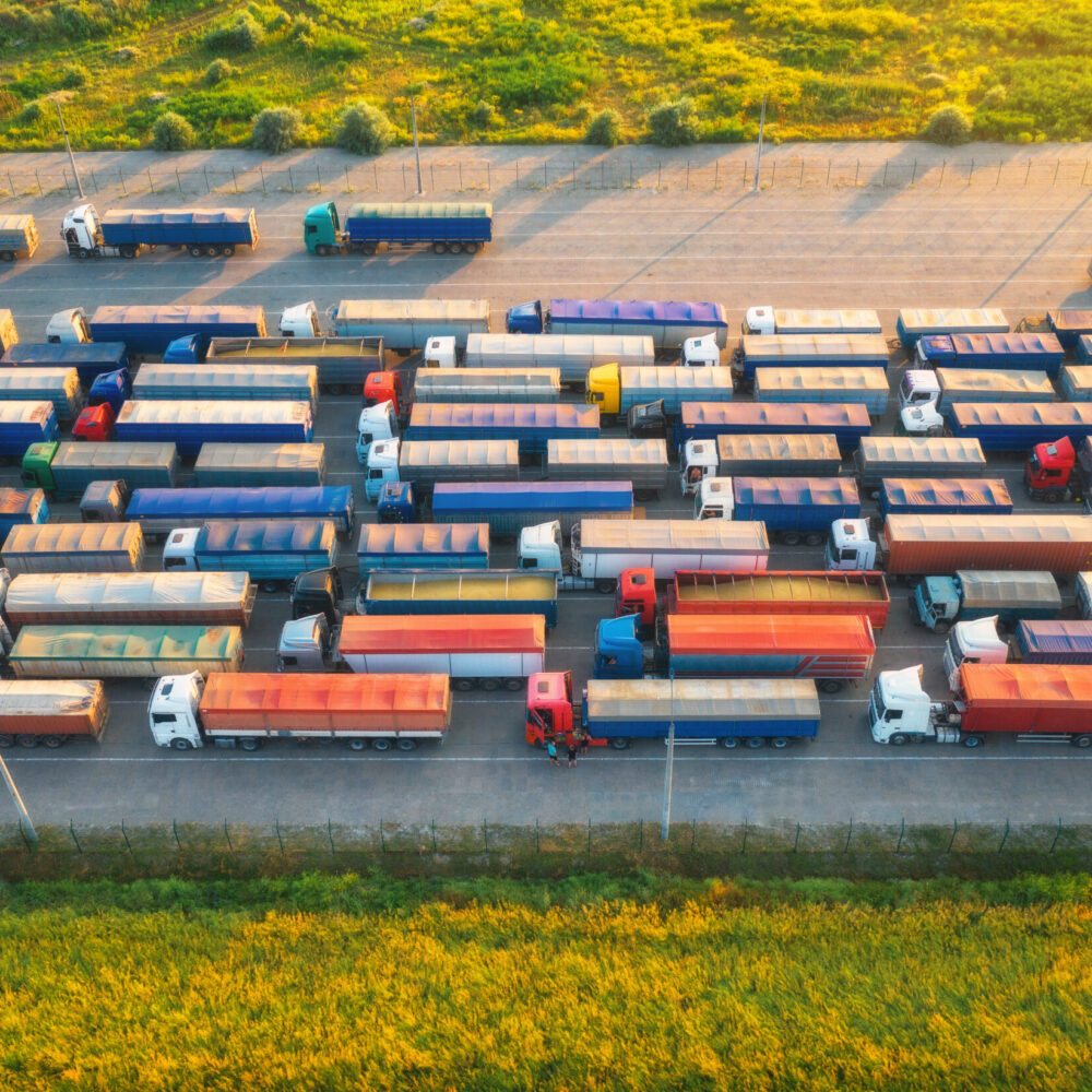 Aerial view of colorful trucks in terminal at sunset in summer. Top view of logistic center. Heavy industry. Transportation. Cargo transport, shipping. International trucking. View from drone of truck
