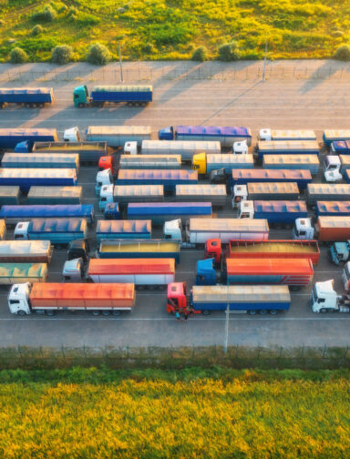 Aerial view of colorful trucks in terminal at sunset in summer. Top view of logistic center. Heavy industry. Transportation. Cargo transport, shipping. International trucking. View from drone of truck