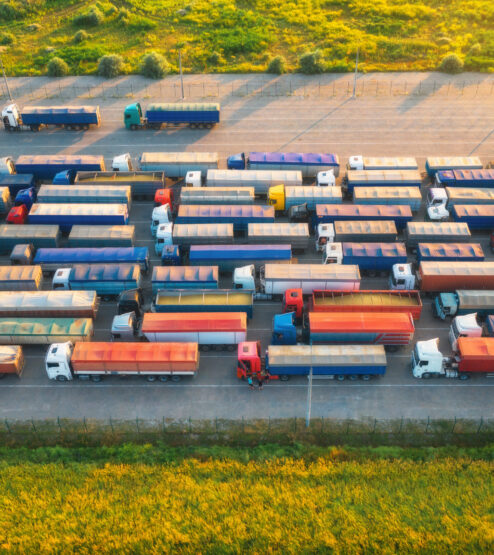 Aerial view of colorful trucks in terminal at sunset in summer. Top view of logistic center. Heavy industry. Transportation. Cargo transport, shipping. International trucking. View from drone of truck