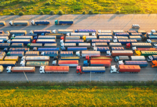 Aerial view of colorful trucks in terminal at sunset in summer. Top view of logistic center. Heavy industry. Transportation. Cargo transport, shipping. International trucking. View from drone of truck