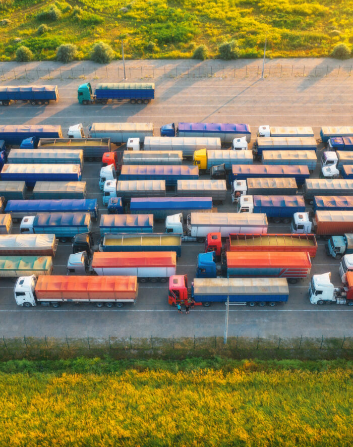 Aerial view of colorful trucks in terminal at sunset in summer. Top view of logistic center. Heavy industry. Transportation. Cargo transport, shipping. International trucking. View from drone of truck
